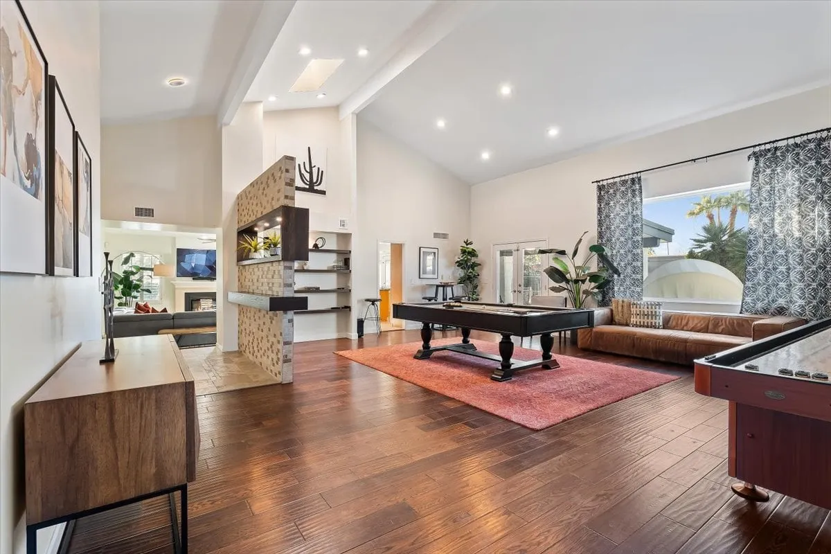 A lively interior game room with a pool table, comfortable sofa, and large windows letting in natural light. This inviting space is perfect for friendly competitions and group entertainment after a day outdoors.