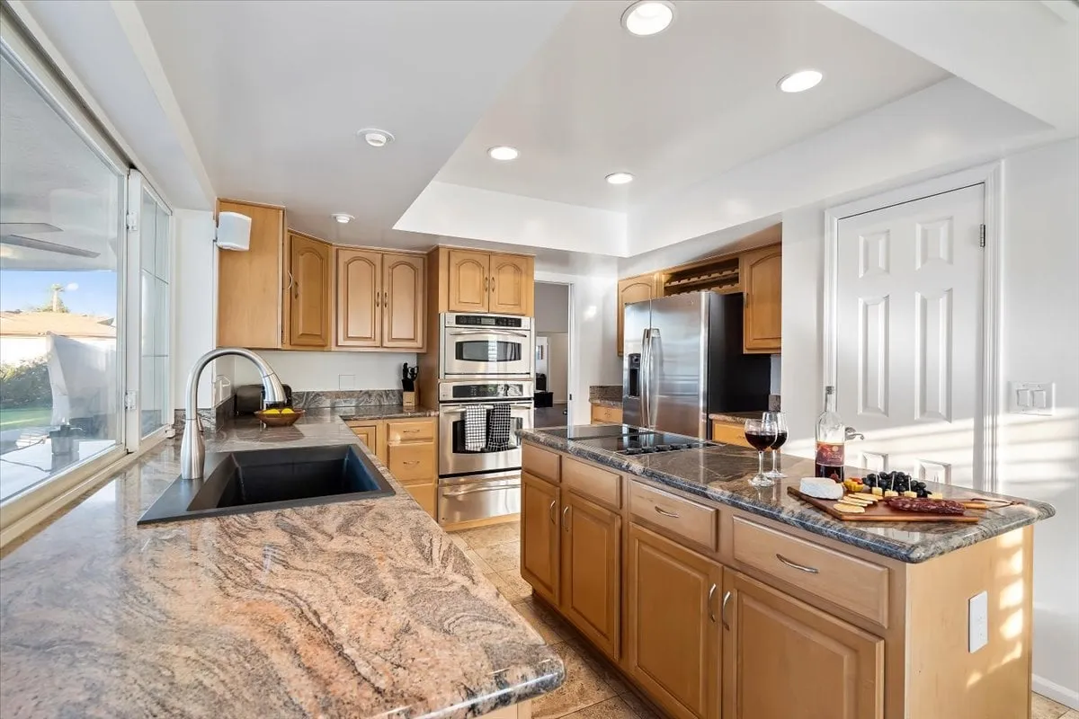 A cozy and functional kitchen scene featuring a granite countertop and island, stainless steel appliances, and a setup for entertaining guests with wine glasses and a platter. The space exudes warmth and is ideal for both everyday meals and special occasions.