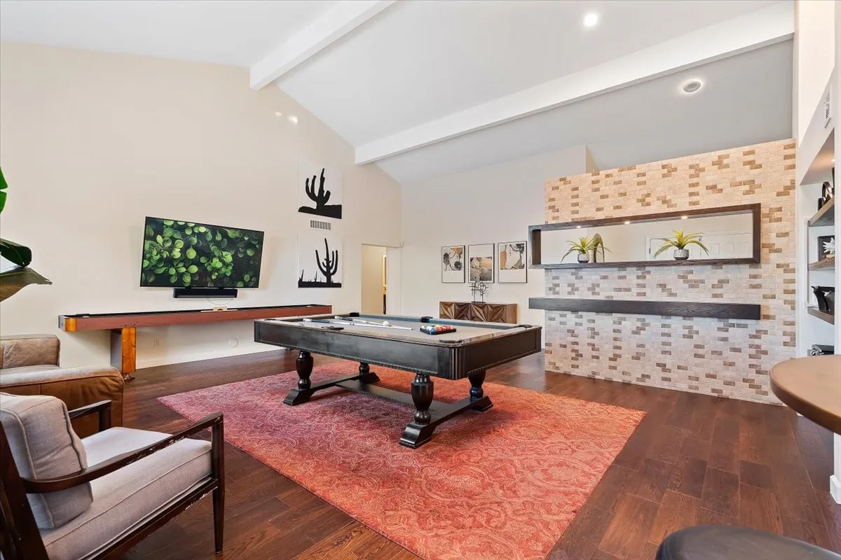 A vibrant game lounge featuring a pool table at the center, a wall-mounted television, decorative wall art, and a cozy rug. The space exudes a sense of fun and relaxation, ideal for friendly competition and social gatherings.