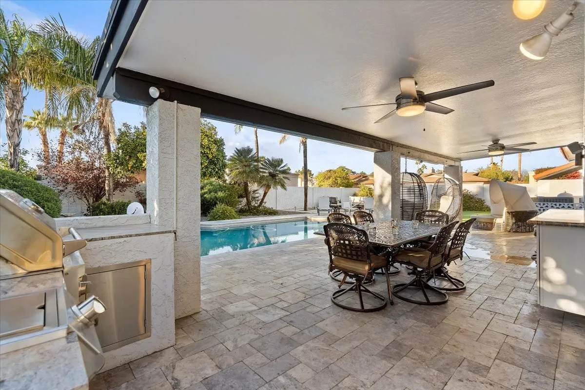 A resort-style backyard featuring a sparkling swimming pool, outdoor dining table, barbecue grill area, and swaying palm trees. The space exudes relaxation and is ideal for après-golf socializing, poolside gatherings, and group barbecues.