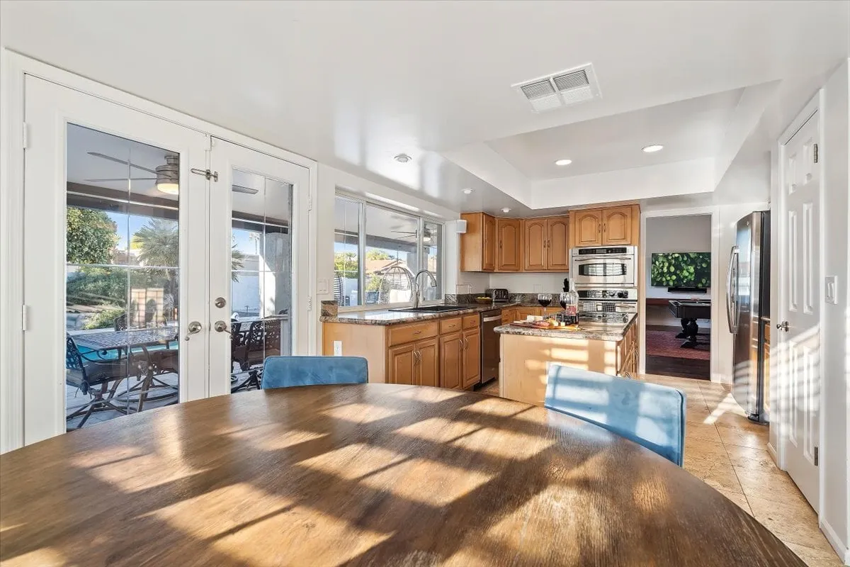 A welcoming dining area with a round wooden dining table, adjacent to a sleek kitchen counter and surrounded by large windows. Stainless steel appliances are visible, and the setup is perfect for hosting family meals, social gatherings, or festive celebrations.