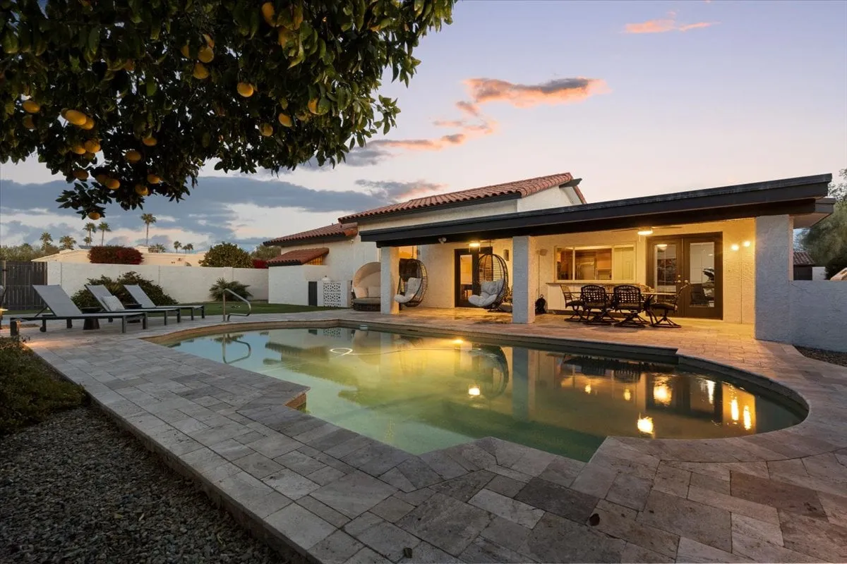 The hero image showcases a serene backyard oasis with a sparkling swimming pool, inviting outdoor seating area, cozy hammocks gently swaying beneath a lush lemon tree, all bathed in the warm glow of the Arizona sunset. The setting is perfect for swimming, lounging, dining al fresco, and enjoying tranquil evenings with friends and family.